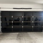 A black glass-paneled garage door in a clean, organized garage with concrete floor and some tools along the left wall.